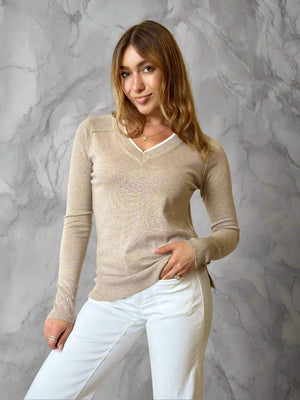 Woman wearing a beige sweater and white pants indoors.