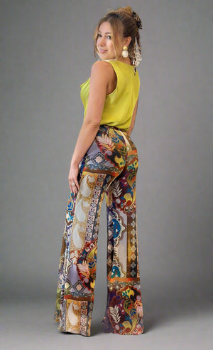 Woman wearing colorful patterned pants and a yellow top in a living room setting.