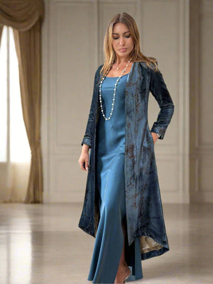Woman in a blue dress with a matching long coat standing in a living room.