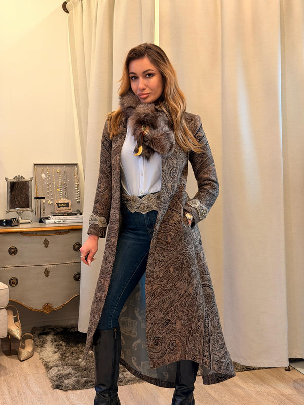 Woman wearing a long patterned coat with fur collar indoors.