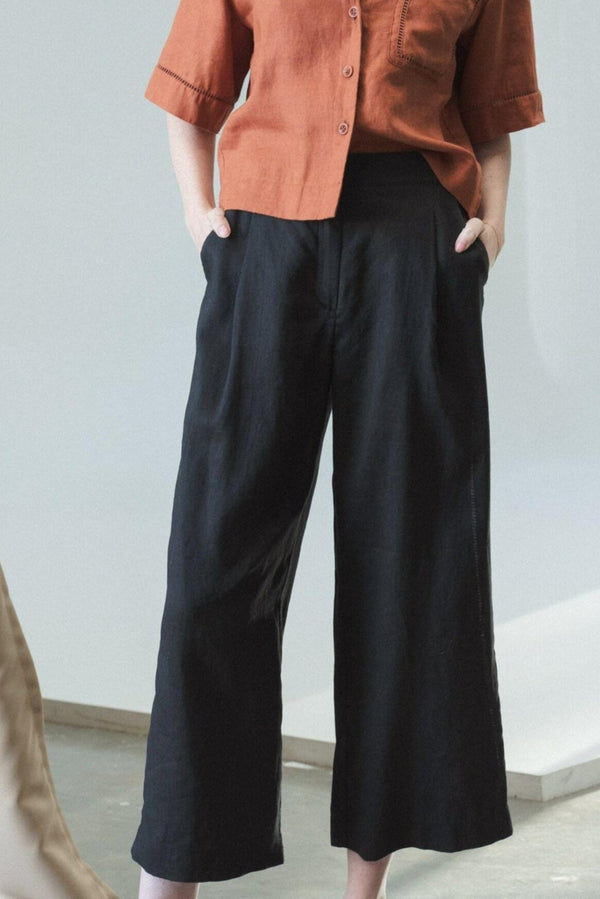 Person wearing a rust-colored shirt and black wide-leg pants against a light gray background