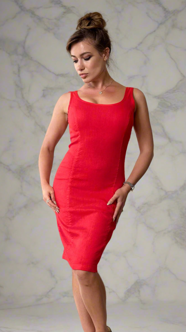 Woman wearing a red dress standing in a room with curtains and a chair.