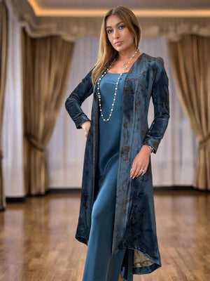 Woman in a blue dress and long coat standing in a living room.