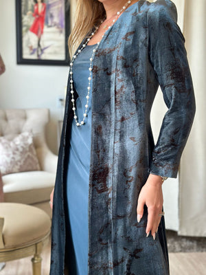 Woman wearing a blue dress with a long, patterned cardigan in a living room setting.