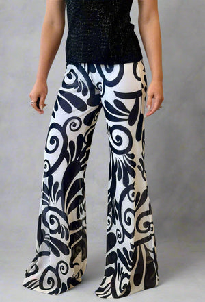 Person wearing black and white patterned pants in a room with wooden floor and white curtain.