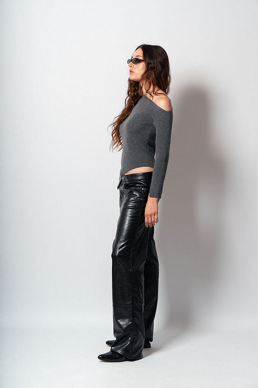 Woman wearing a gray off-shoulder top and black leather pants against a white background